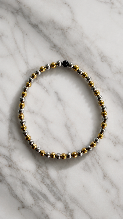 Beaded bracelet with gold, silver, and black beads on a marble surface