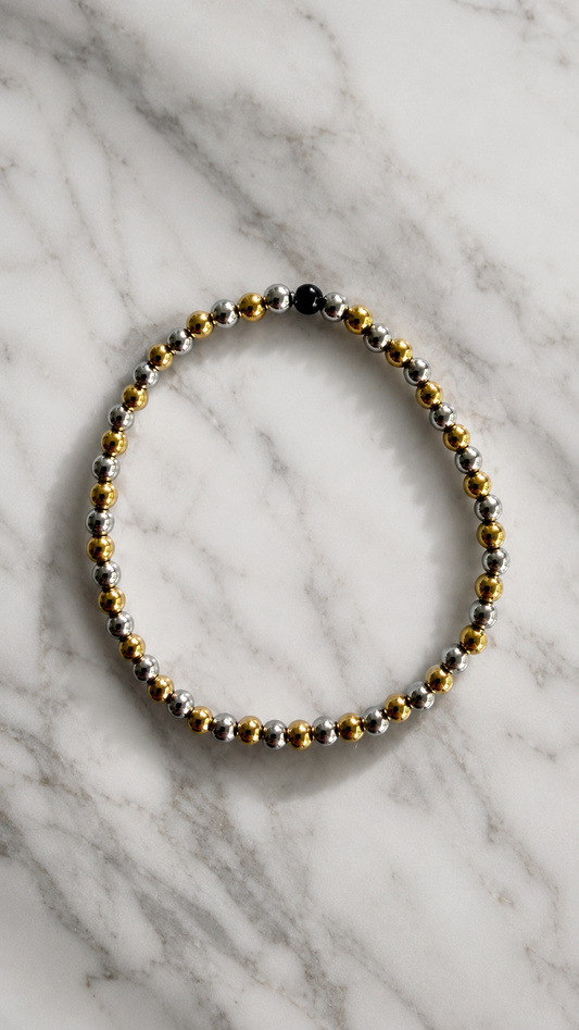 Beaded bracelet with gold, silver, and black beads on a marble surface