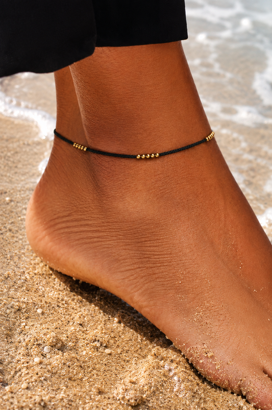 black & gold anklet on a foot with sand in the background