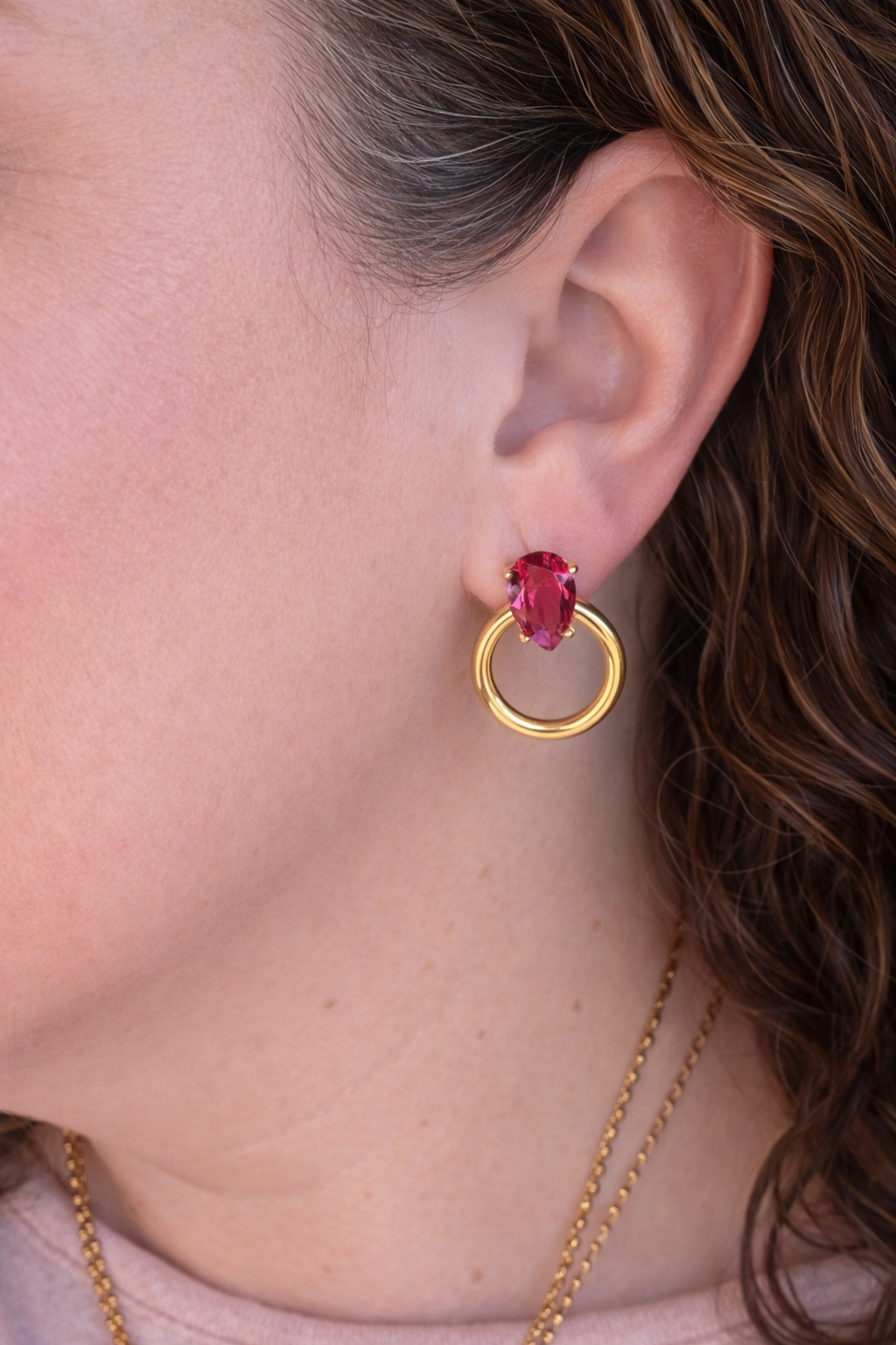 Close-up of a person wearing a gold earring with a red gemstone.