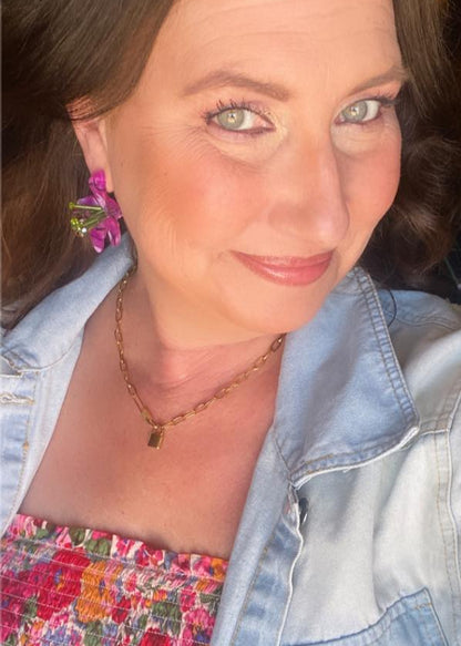 Woman wearing a denim jacket over a floral dress with a colorful earring.