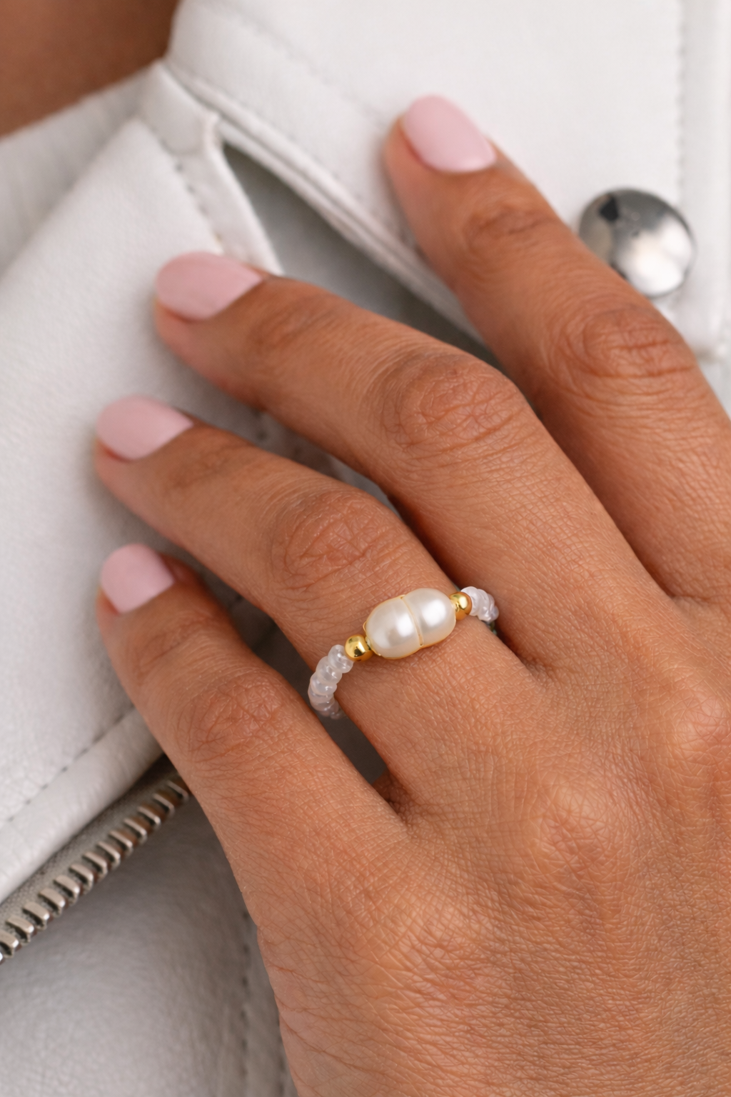 Hand wearing a pearl ring with a blurred background