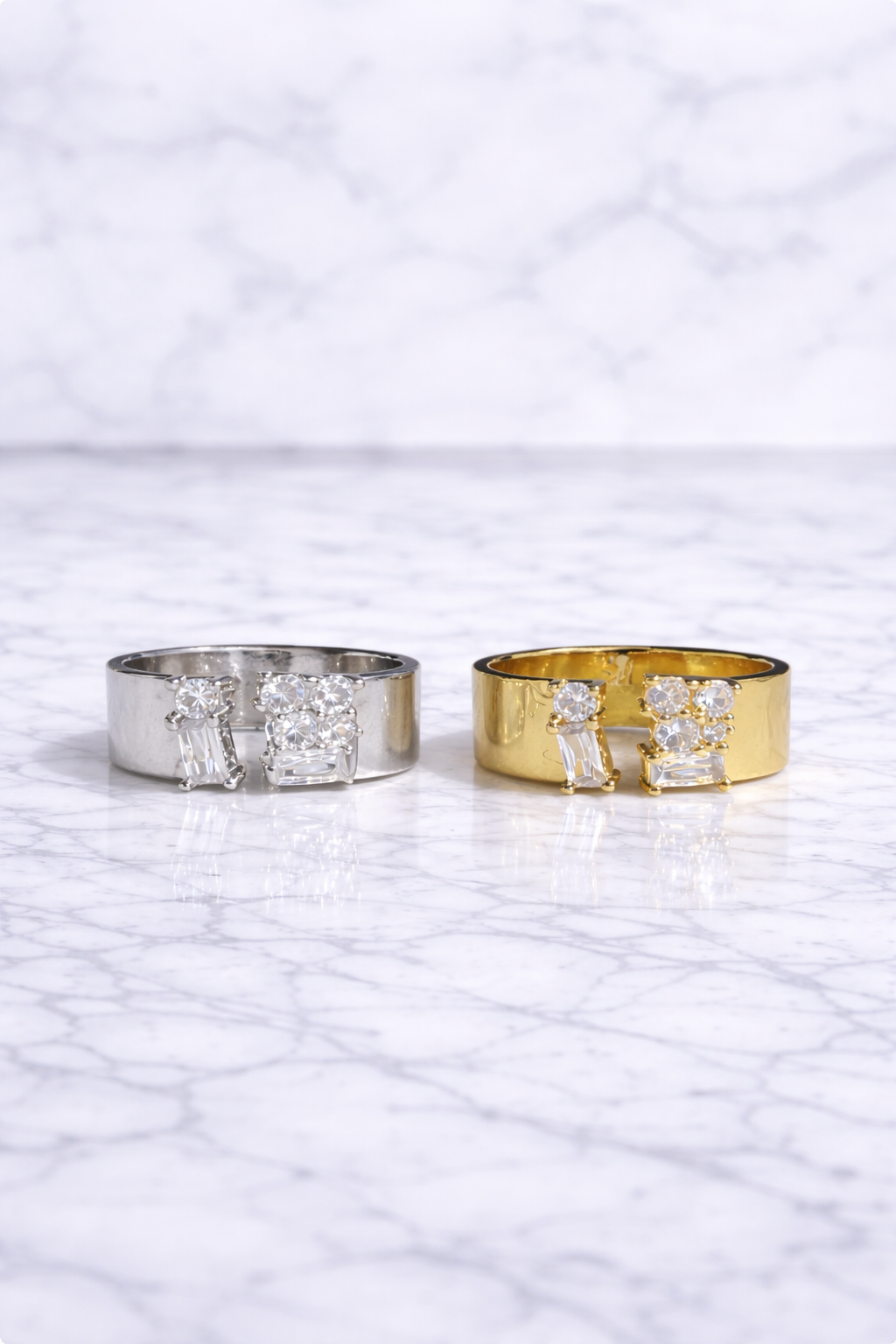 Two diamond rings, one gold and one silver, on a marble surface.