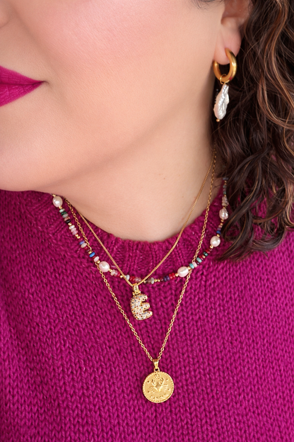 Close-up of a person wearing multiple necklaces and earrings on a pink sweater.