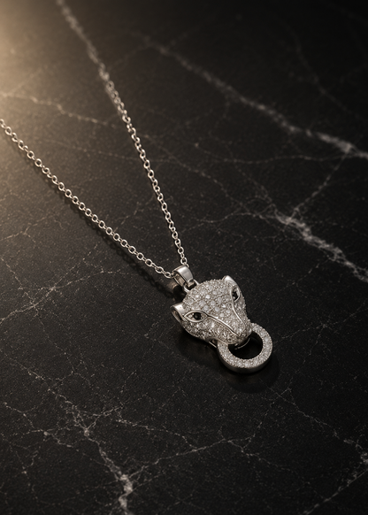 A silver-toned necklace with a panther head pendant paved with clear stones, displayed on a dark black marble surface.