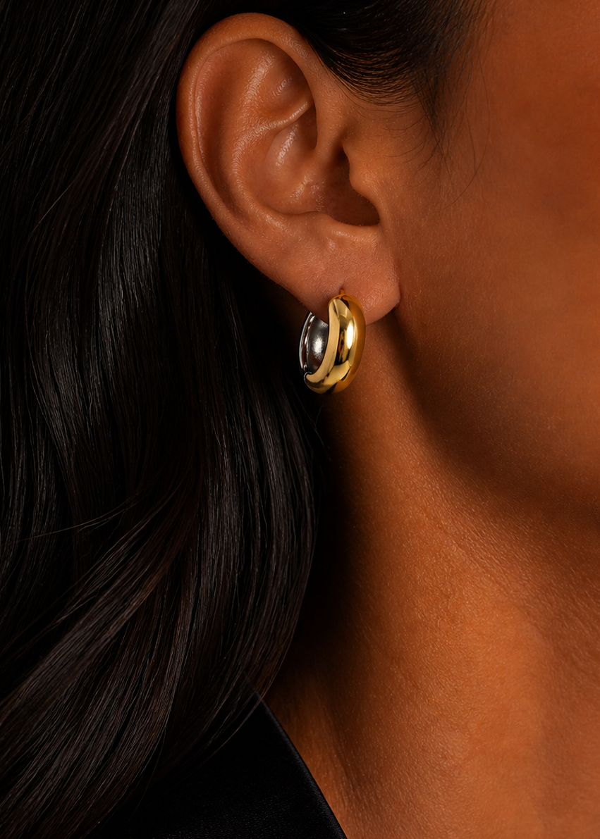 Close-up of an ear wearing a gold hoop earring with a black background