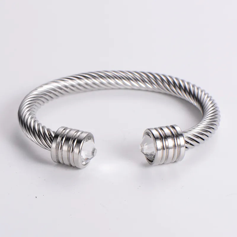 A collection of cuff bracelets with stainless steel and 18kt gold plating, featuring different stone colors, displayed on a textured surface.