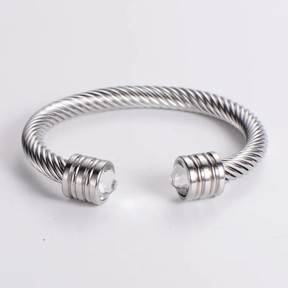 A collection of cuff bracelets with stainless steel and 18kt gold plating, featuring different stone colors, displayed on a textured surface.