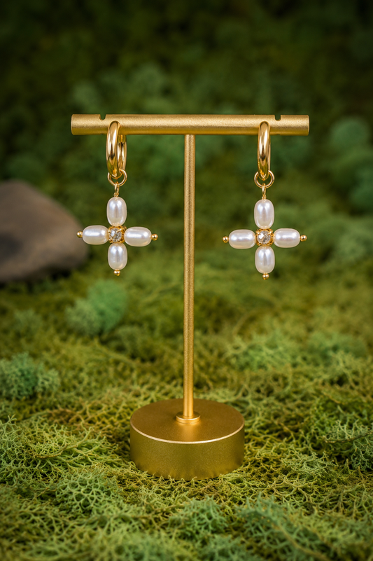 Gold earrings with pearl-like stones on a gold stand against a green natural background