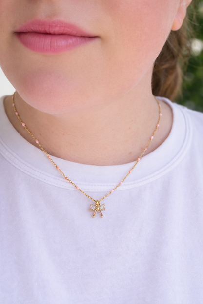 Close-up of model wearing VEITA Jewelry Ava Bow Necklace with gold chain, pink bead accents, and crystal bow pendant