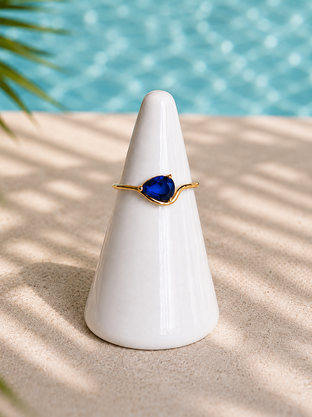 Rosie Ring featuring a pear-shaped cobalt blue zircon stone set in 18kt gold plating displayed on a white ceramic ring cone.