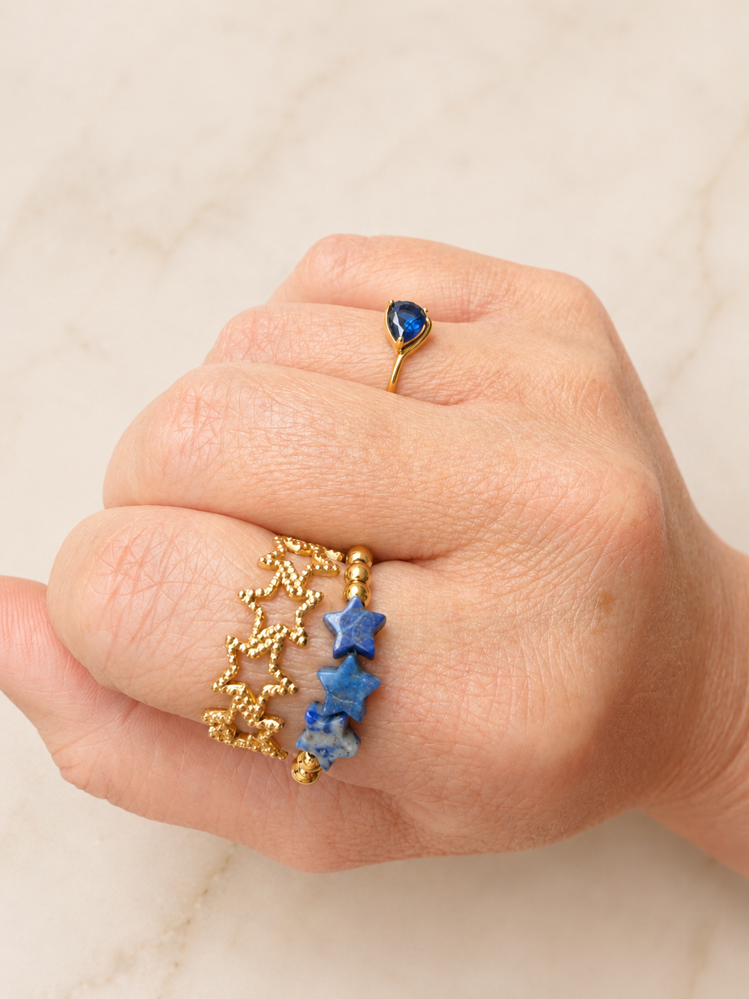 Close-up of a hand wearing VEITA ring stack: Betsy Stretch Gemstone Ring and Textured Star Ring on index finger and Rosie Ring on ring finger.