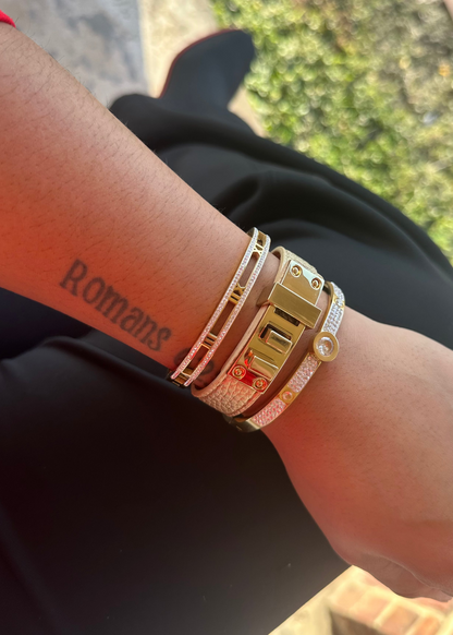 Close-up of a wrist with multiple gold bracelets and a tattoo on a blurred outdoor background